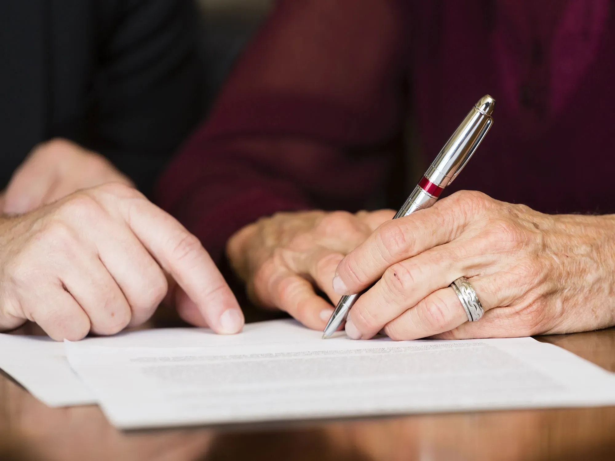 Personne âgée guidée pour signer un document officiel.