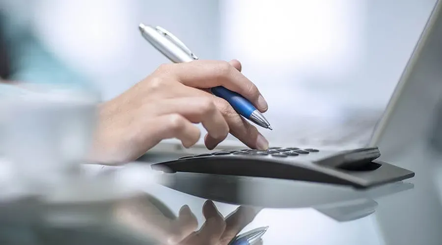 Gros plan sur l'utilisation d'une calculatrice de bureau avec un stylo à la main.