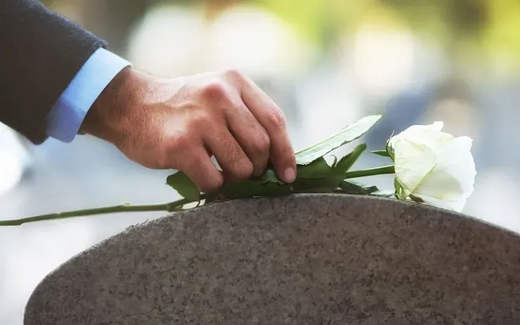 Main déposant une rose blanche sur le sommet d'une pierre tombale.