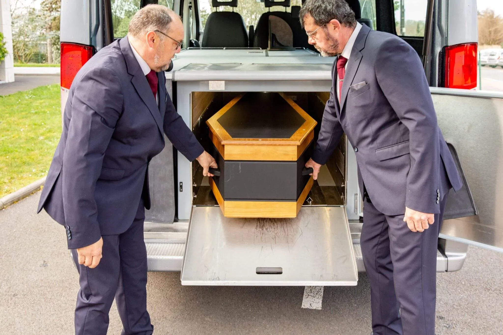 Deux agents funéraires chargeant un cercueil dans un véhicule.