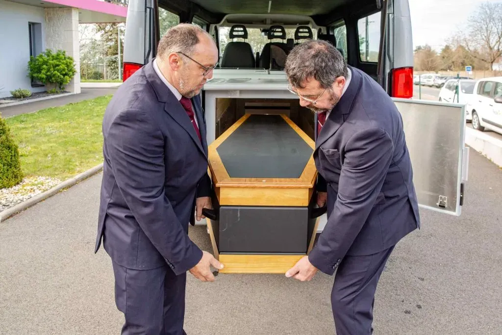 Deux agents funéraires chargeant un cercueil dans un véhicule.